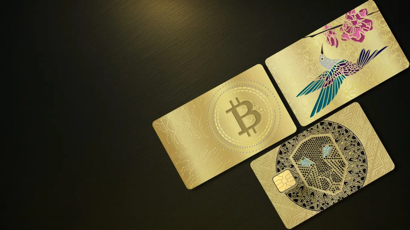 Luxurious gold-themed cryptocurrency and NFT credit cards featuring Bitcoin, a colorful hummingbird, and an intricate skull design set against a black background.